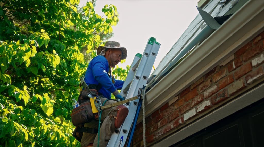 Eminent Roofing crew member on a ladder inspecting a Kennewick home roof and gutter line
