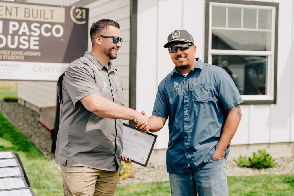Eminent Roofing team members shaking hands with a framed certificate at a Tri-Cities community event